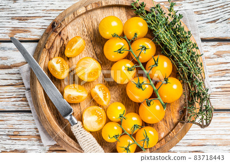 Sliced yellow cherry tomato on a wooden tray with herbs. White wooden background. Top view Sliced yellow cherry tomato on a wooden tray with herbs. White wooden background. Top view 83718443