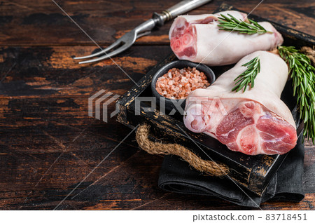 Uncooked Raw pork hoof, knuckle, feet in a wooden tray with herbs. Wooden background. Top view. Copy space Uncooked Raw pork hoof, knuckle, feet in a wooden tray with herbs. Wooden background. Top view. Copy space 83718451