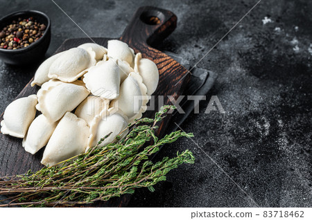 Frozen raw dumplings pierogi with potato on a wooden board. Black background. Top View. Copy space 83718462