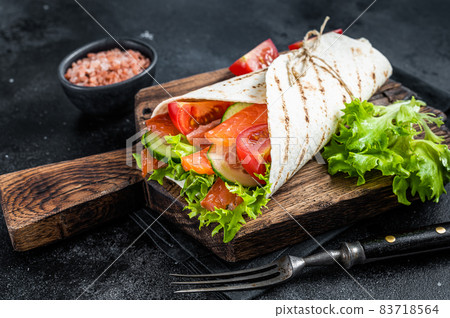 Tortilla Wrap salmon roll with salad, vegetables. Black background. Top view 83718564