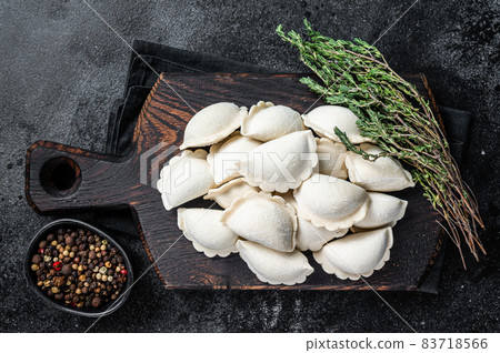 Frozen raw dumplings pierogi with potato on a wooden board. Black background. Top View 83718566
