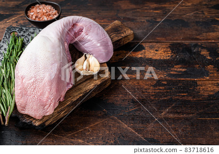 Uncooked Raw beef or veal tongue on butcher board with meat cleaver. Dark wooden background. Top view. Copy space Uncooked Raw beef or veal tongue on butcher board with meat cleaver. Dark wooden background. Top view. Copy space 83718616