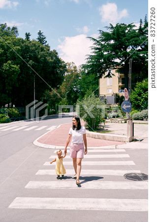 Mom leads the girl along the zebra crossing across the road 83727260