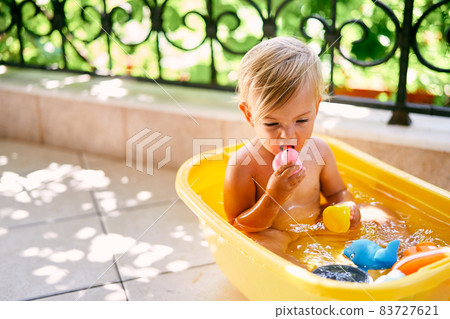 Small child sits in a basin of water and gnaws a rubber duck Small child sits in a basin of water and gnaws a rubber duck 83727621
