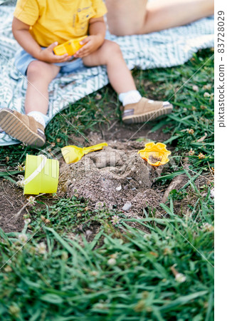 Legs of a toddler sitting on a blanket on a green lawn next to toys Legs of a toddler sitting on a blanket on a green lawn next to toys 83728029