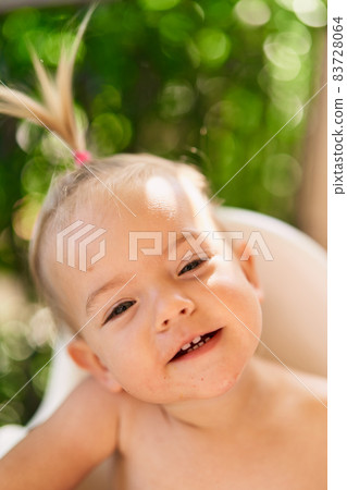 Smiling little girl with a ponytail sits on a high chair. Portrait Smiling little girl with a ponytail sits on a high chair. Portrait 83728064