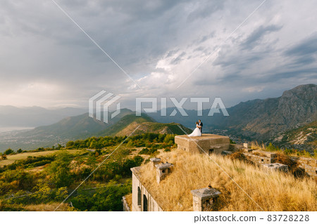 The bride and groom hold hands on the roof of the Gorazda fort, behind them a view of the Bay of Kotor 83728228