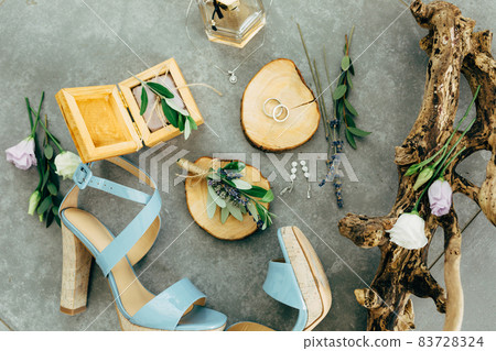Wedding rings lie in a wooden stand surrounded by sandals with heels, wooden box, perfume, flowers and twigs on the floor Wedding rings lie in a wooden stand surrounded by sandals with heels, wooden box, perfume, flowers and twigs on the floor 83728324
