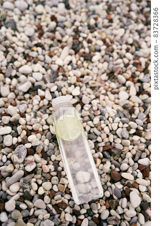Bottle of water with a slice of lime lies on a pebble beach 83728366