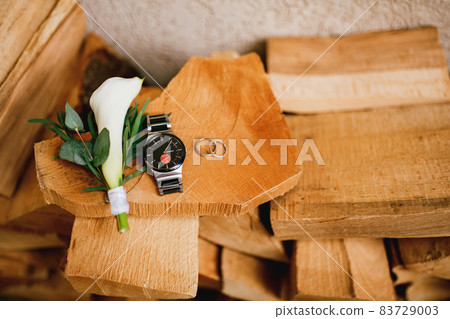 Wooden logs against the wall with wedding rings, a man's wristwatch and a calla flower boutonniere. 83729003