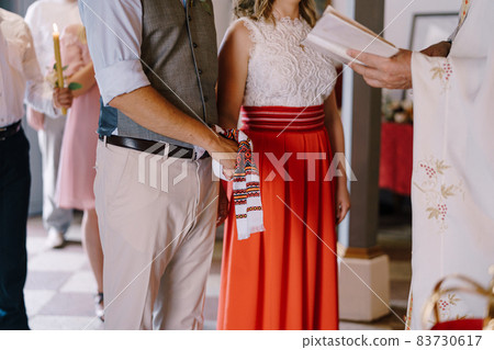 Bride and groom with their hands tied with a towel in front of the priest. Close-up 83730617