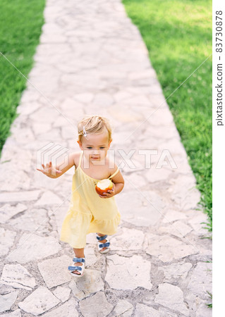 Little girl with an apple in her hand walks along a cobbled path in the green grass. View from above 83730878