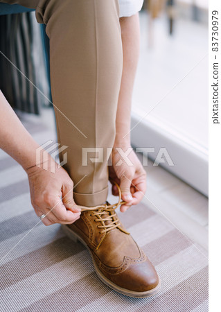 Groom tightens the laces on the brown brogues. Close-up 83730979