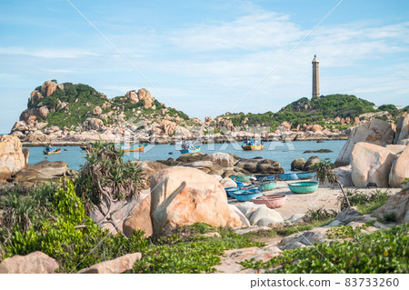 Scenic view of the lighthouse on the beautiful shore with large stones. View of the bay with crystal water. Colourful vietnamese fishing boats. Scenic view of the lighthouse on the beautiful shore with large stones. View of the bay with crystal water. Colourful vietnamese fishing boats. 83733260