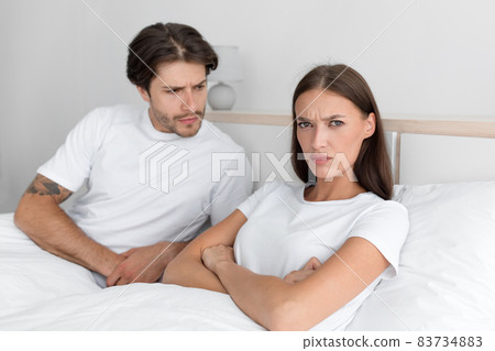 Unhappy millennial european guy calm offended woman with crossed hands on chest on bed in bedroom interior Unhappy millennial european guy calm offended woman with crossed hands on chest on bed in bedroom interior 83734883