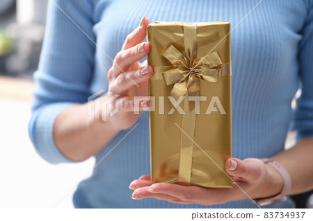 Woman holding a gift in golden wrapping paper Woman holding a gift in golden wrapping paper 83734937