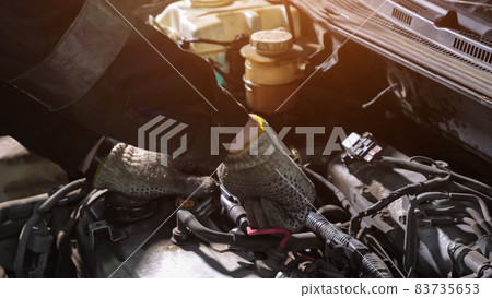 Mechanic in gloves unscrews detail of broken automobile 83735653