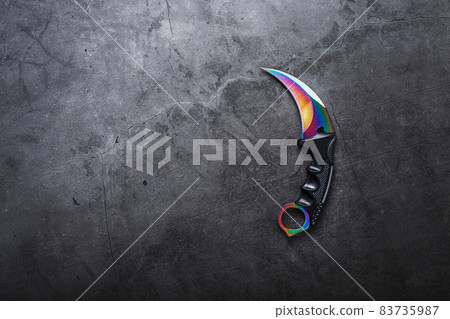 Kerambit dagger with a rainbow-colored blade on a dark textured background. 83735987