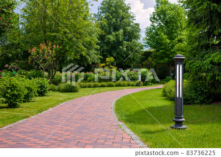 lantern iron ground garden lighting of a park path paved with stone tiles in the backyard among plants, bushes and trees surrounded by a green lawn on a sunny summer day, nobody. lantern iron ground garden lighting of a park path paved with stone tiles in the backyard among plants, bushes and trees surrounded by a green lawn on a sunny summer day, nobody. 83736225