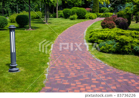lantern iron ground garden lighting of a park path paved with stone tiles in the backyard among plants, bushes and trees surrounded by a green lawn on a sunny summer day, nobody. lantern iron ground garden lighting of a park path paved with stone tiles in the backyard among plants, bushes and trees surrounded by a green lawn on a sunny summer day, nobody. 83736226