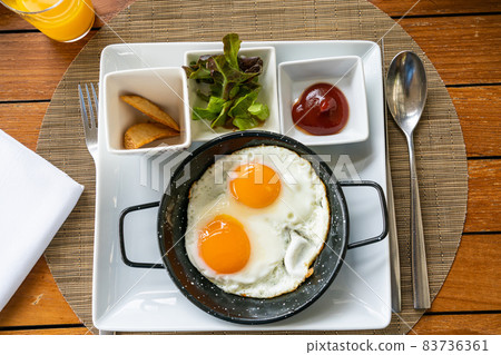 Breakfast - Sunny side up fried eggs with tomato sauce and potato wedges. 83736361