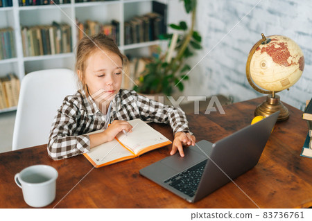 High-angle view of happy focused Caucasian school girl studying with books laptop preparing for test exam writing essay doing homework at home. 83736761