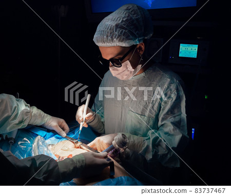 A woman surgeon in 3D glasses operates the patient's body A woman surgeon in 3D glasses operates the patient's body 83737467