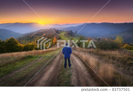 Man on the rural dirt road on the hill looking on mountain in fog 83737501