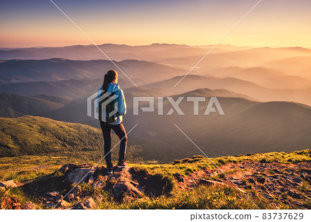 Girl with backpack on mountain peak with green grass at sunset 83737629