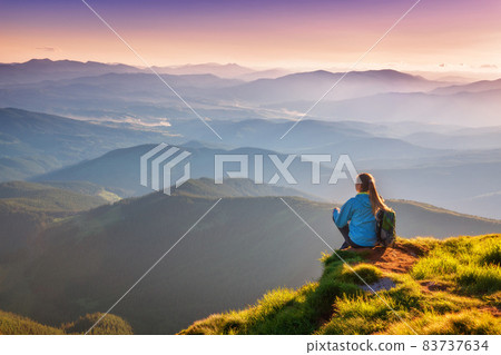 Young woman with backpack sitting on the mountain peak 83737634