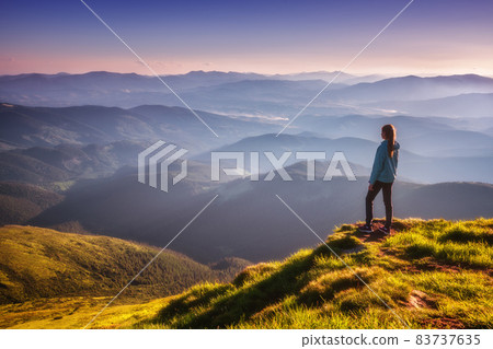 Girl on mountain peak with green grass looking in mountains Girl on mountain peak with green grass looking in mountains 83737635