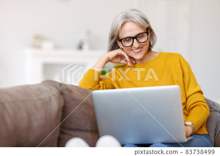Portrait of happy smiling senior woman resting relaxing on sofa with laptop at home Portrait of happy smiling senior woman resting relaxing on sofa with laptop at home 83738499