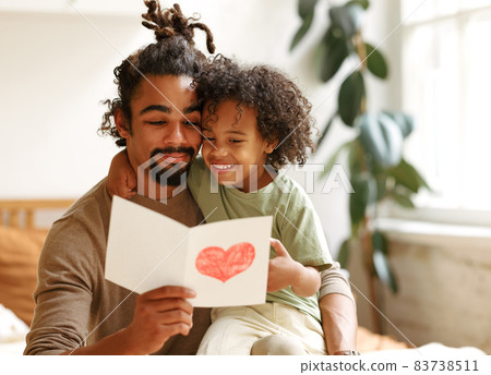Cute african american little boy son giving his father handmade greeting postcard on Fathers Day Cute african american little boy son giving his father handmade greeting postcard on Fathers Day 83738511