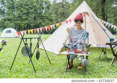 Young woman baking pancakes at a campsite 83738637