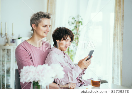 Portrait of happy couple man and woman using smartphone while sitting at the table together during breakfast in the kitchen at home. Scrolling social networks, chatting, watching videos. 83739278