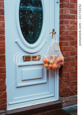 Reusable string bag from environmentally friendly materials with citrus fruits and blank card hanging on the door handle. Local farmer healthy food delivery. Zero-waste, plastic-free lifestyle. 83739292