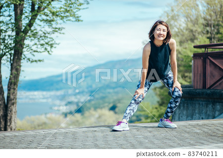 A woman doing preparatory exercise in the park (bending and stretching / smiling) 83740211