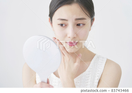 一個女人用手鏡看著她的臉 83743466