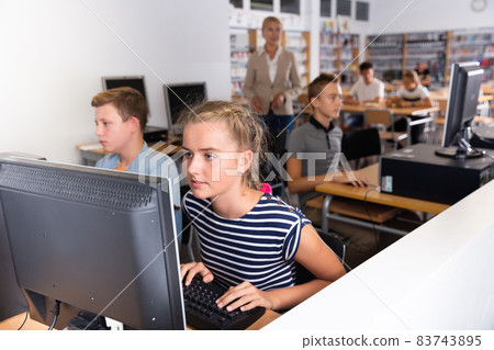 Schoolgirl using computer at lesson, teacher teaching pupils 83743895