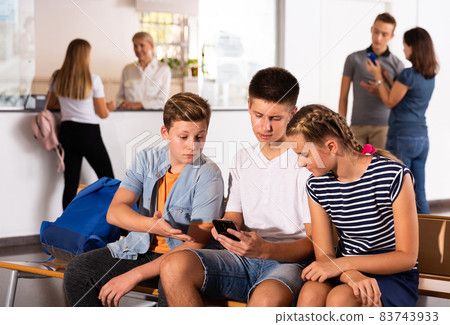 Girl and boys using phones, have rest between lessons Girl and boys using phones, have rest between lessons 83743933