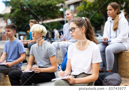 Students record lecture while sitting on a stone street parapet Students record lecture while sitting on a stone street parapet 83743977