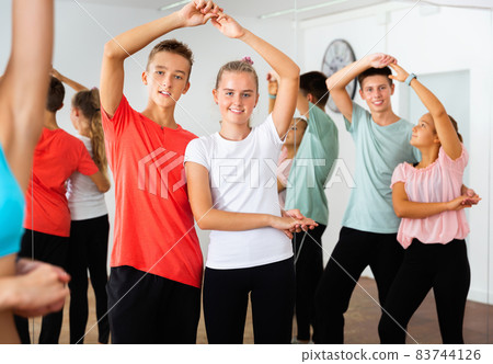 Group of teenage boys and girls training movements of slow foxtrot in dance studio with female coach 83744126