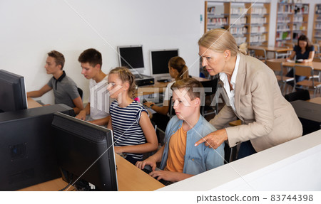 Schoolchildren using computers and teacher teaching them 83744398