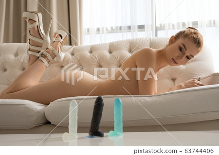 Naked woman lying in room with sex toys 83744406