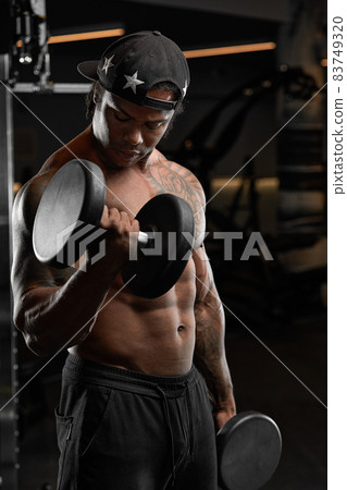 Strong and muscular dark skin man trains on modern equipment in gym. Portrait of muscular pumped up fitness trainer 83749320