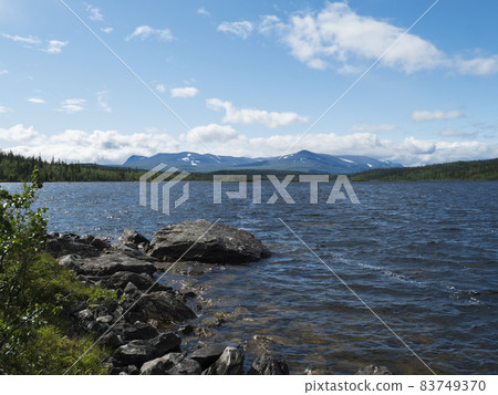 View over lake Stuor Dahta in Laponia. Sweden Lapland nature. Mountains, birch trees, spruce forest, rock boulders and grass. Sky, clouds and clear water. 83749370