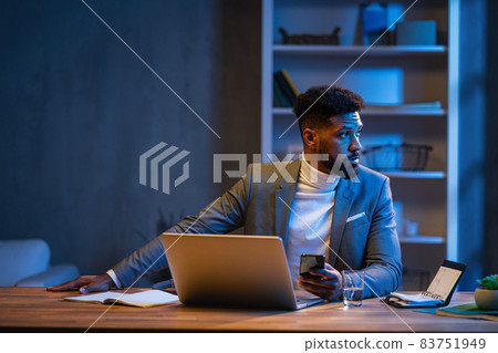 Young african american businessman working indoors in office at night. Young african american businessman working indoors in office at night. 83751949