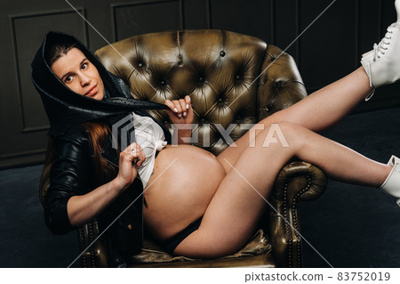 a pregnant woman in black clothes and a headscarf lies on a chair in the studio on a dark background 83752019