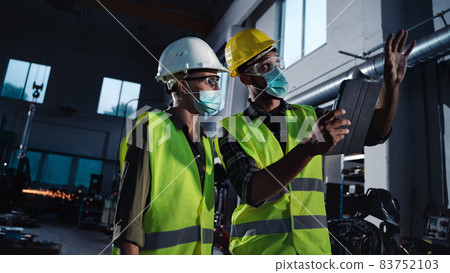 Industrial inspectors with face masks doing general check up at metal workshop, coronavirus concept 83752103