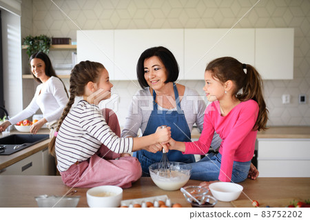 Happy small girls with mother and grandmother making pancake mixture indoors at home, cooking. 83752202